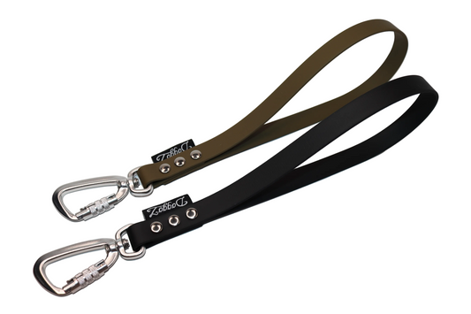 A pair of short BioThane dog leash handles in Olive Green and Black, each featuring a silver locking carabiner, heavy-duty silver rivets, and the DoggoZ brand label.