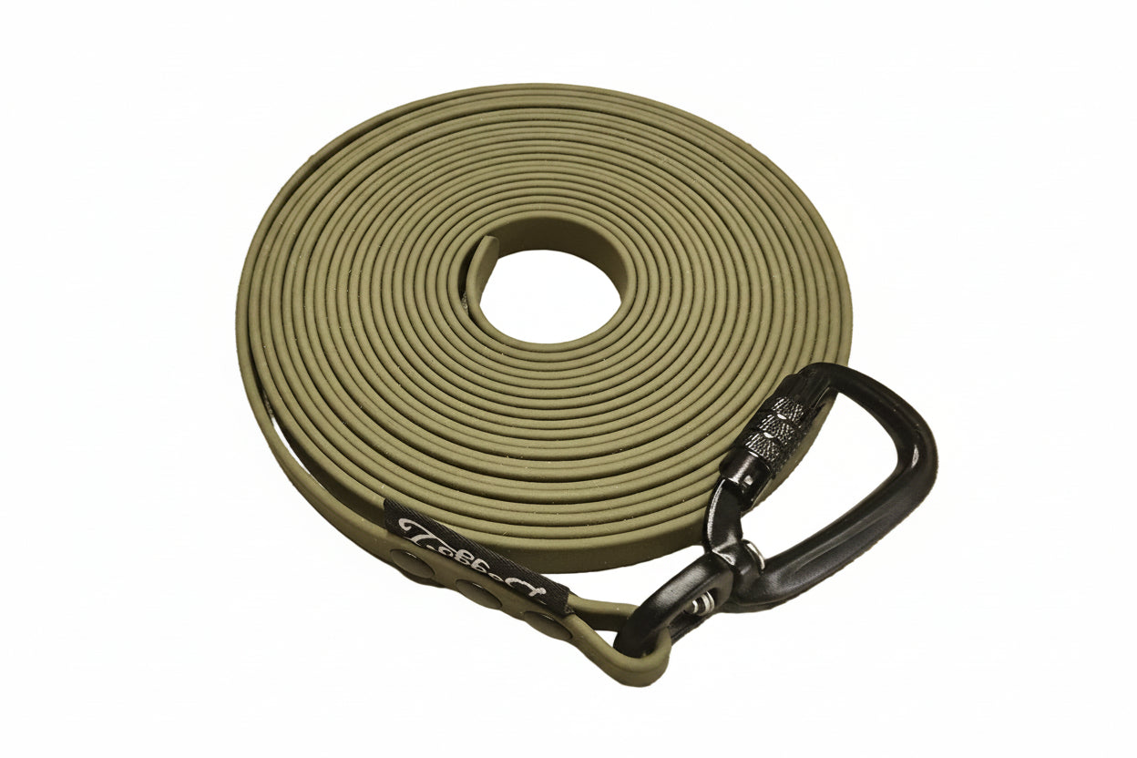 A tightly coiled olive green BioThane drag line 5 meter - 10 meter. Features a robust black auto-locking carabiner, rivets, and a black DoggoZ tag on a pure white background, illustrating the full length range available for customization.