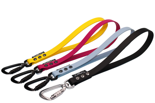 Four BioThane traffic handles in Yellow Sunflower, Pink Magenta, Blue Husky Eyes, and Black, each featuring a locking carabiner, heavy-duty rivets, and the DoggoZ brand label.