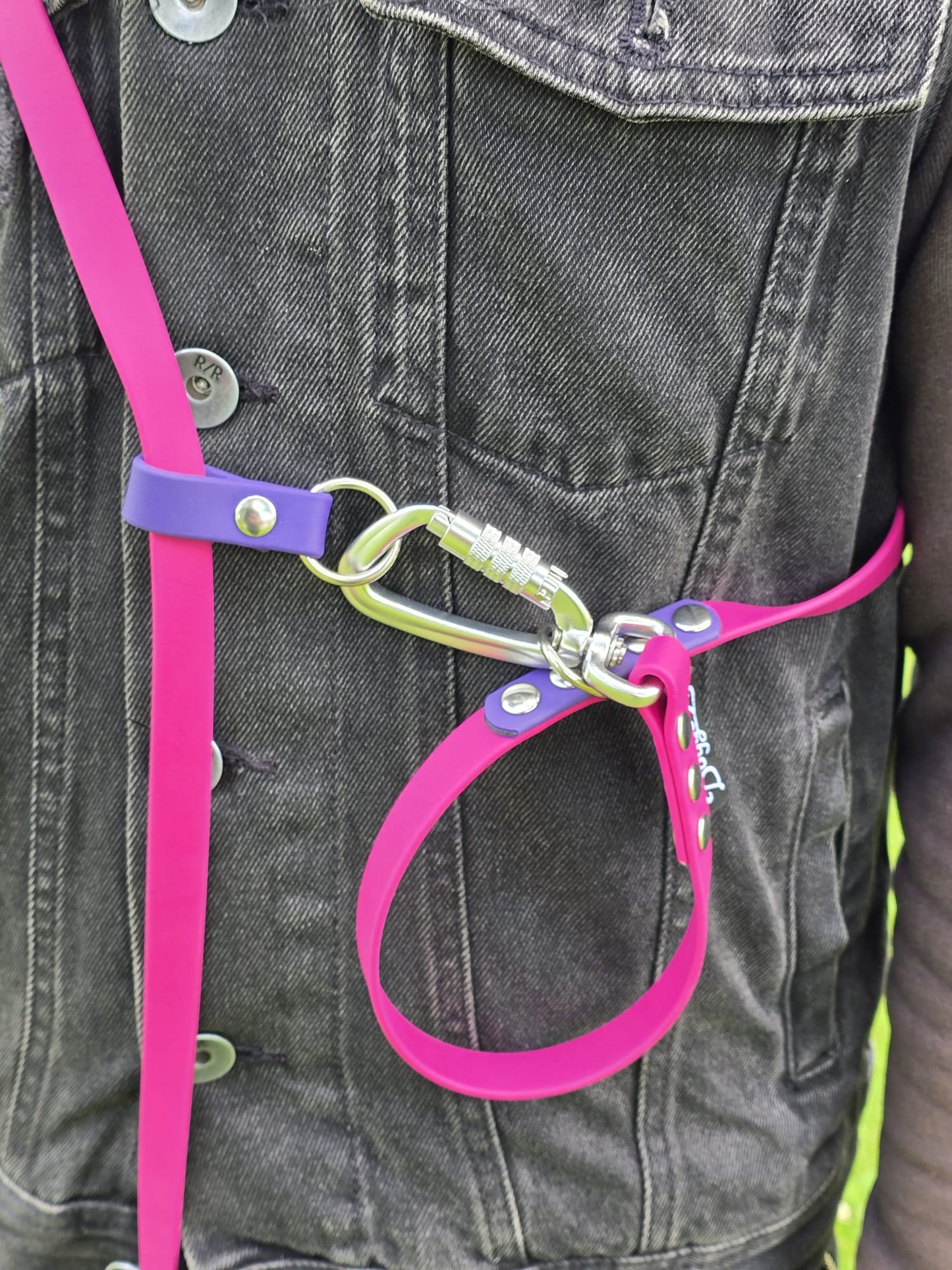Close-up of the DoggoZ hands-free BioThane dog leash in pink, worn over a denim jacket. The silver carabiner is looped through the rings to shorten the leash length.