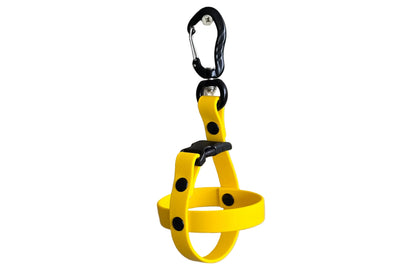 A clean studio photograph on a white background showing a single handcrafted yellow BioThane dog ball holder. The holder is formed by a crisscross BioThane strap secured by sturdy black rivets. At the top, a quick-release black buckle connects to a heavy-duty black aluminum carabiner with a swivel action and a screw-lock mechanism. The design illustrates a durable, easy-to-clean, and secure way to carry fetch balls hands-free. Note that no balls are included in Horizon.