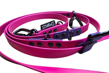 Close-up of a 2-tone hands-free adjustable BioThane dog leash in magenta pink with violet purple accents. Shows premium black auto-lock carabiners, black tactical rings, heavy-duty rivets, and a stitched DoggoZ brand tag on a clean white background.