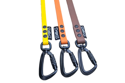 A selection of DoggoZ handleless BioThane drag lines in yellow, orange, and brown. The photo showcases the high-quality matte finish of the BioThane material, paired with heavy-duty black locking carabiners and durable rivets. These snag-resistant leashes are designed to give dogs freedom during hiking and off-leash training while ensuring safety.
