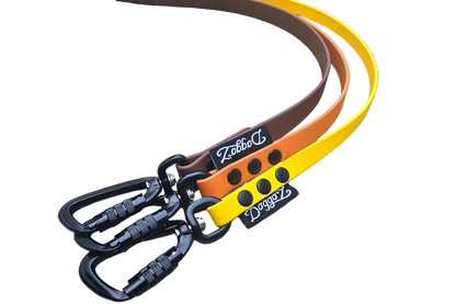 Three DoggoZ handleless BioThane drag lines in yellow, orange, and brown colors. The image shows the premium matte finish of the straps, heavy-duty black locking carabiners, and the DoggoZ brand label. These leashes are specifically designed for snag-resistant hiking and training adventures.